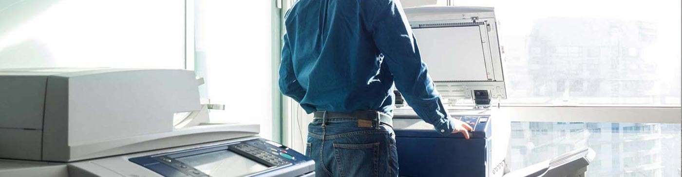 man standing in front of a printer looking out a window overlooking the city